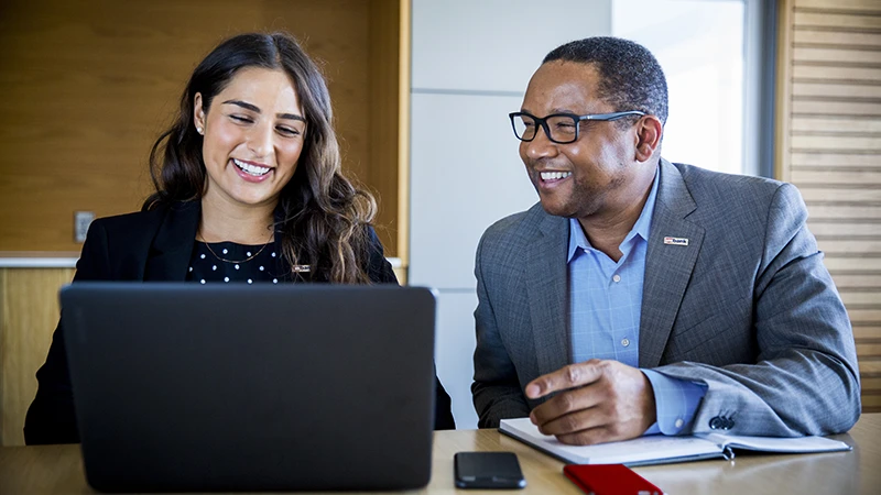 Two professionals looking at a laptop and smiling as they research global corporate trust.
