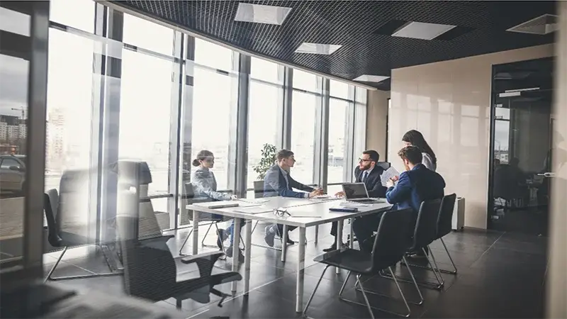Large corporate board room with many windows and 5 people inside at a table