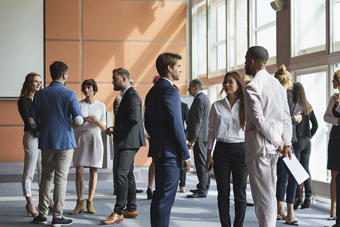 15 professional bankers standing in a large building talking to each other about US banks in Europe